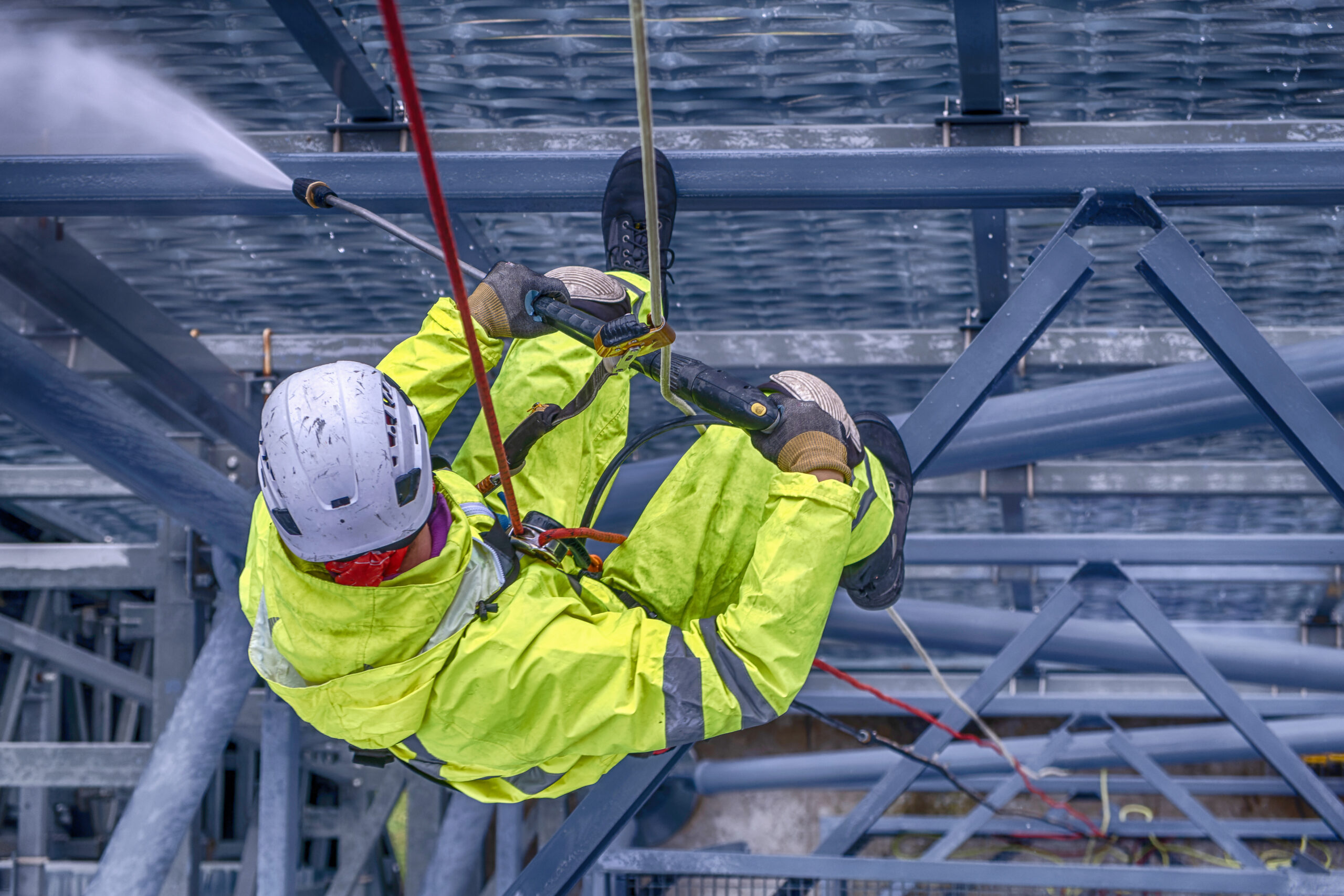 Looking down on rope-access technician power washing fenced-in structure