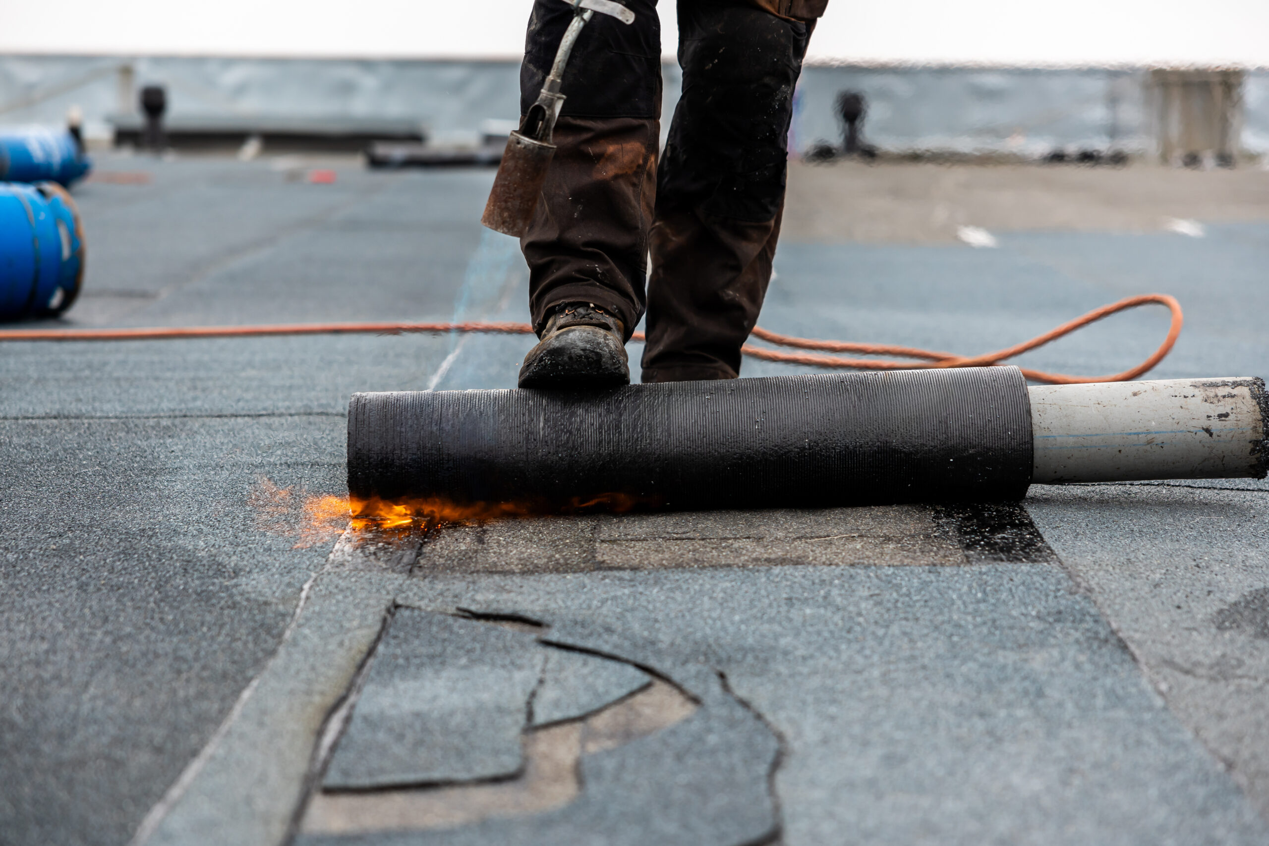 Professional roofer at work securing rolled tar paper with a blowtorch on a flat roof installation process